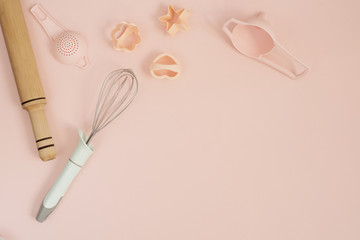 Cookie cutters, whisk, roller pin and kitchen bake tools for making sweets. Pastel pink background. Top view of a holiday baking still life