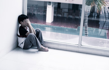 Depressed young boy on the floor by the wall near window, out focus