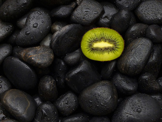 Obraz na płótnie Canvas Kiwi ist auf schwarzen steinen mit Wassertropfen 