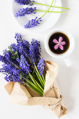 A cup of espresso and a bouquet of purple flowers in kraft paper on a white background. Flower decoration. Flat lay. Creative layout