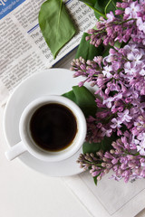 A cup of coffee and a bouquet of fresh lilacs on the background of the newspaper. Lifestyle. Flat lay
