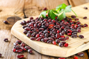 Red raw beans with greens on a wooden table.