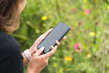 Asian woman wearing smartwatch and using smartphone in her vacation time at green field in selective focus.