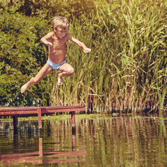 Little boy having fun and jumping into the river from pier, image with square aspect ratio and warm...