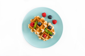 Traditional belgian waffles with blueberries and raspberries, isolated on white background. Top view.

