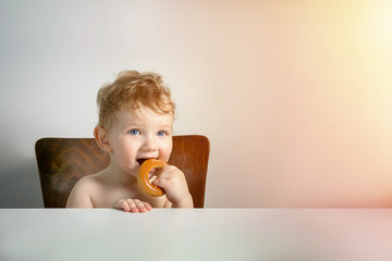 Baby chews the bagel and waits for dinner at the table.  closeup