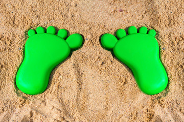 Fototapeta na wymiar Footprint on the sand in the form of a green shape, the concept of moving forward and travel and tourism with a copy space