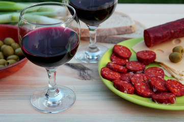 Food and beverages - still life - two glasses of red wine on a table with sliced salami, cheese, bread and green olives