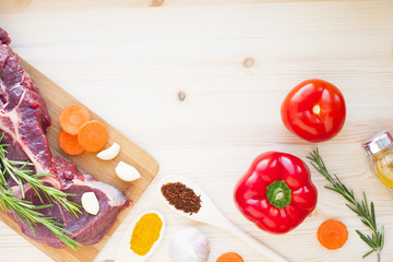 Raw beef meat on the wooden cutting board with vegetables, rosemary and spices. Top view. Close up. Food concept.