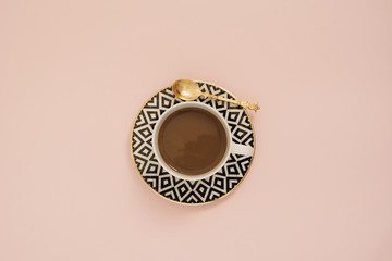 Coffee on a pastel punchy pink background.  Latte in a white, black and gold coffee cup. Feminine workplace concept. Freelance fashion comfortable femininity workspace with coffee