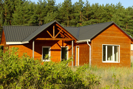 Wooden House In Countryside. Ecological Small Wooden House. Wooden House With Meadow In Front Of It. Beautiful Modern Wooden House, Front Elevation. Front View.
