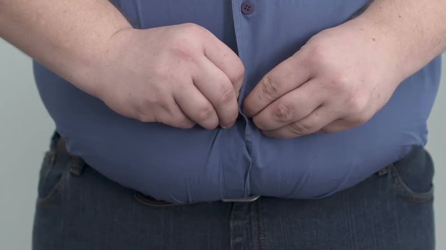 Fat man making lot of effort to button up his shirt on huge paunch, obesity