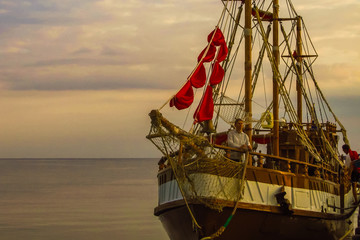 A ship with red sails lowered by a wooden pier