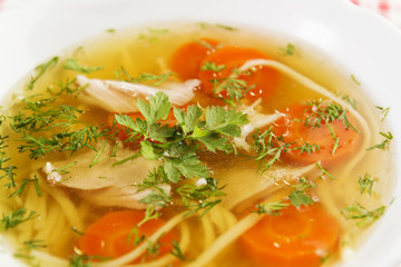 Chicken soup or broth with noodels, chicken meat pieces , carrot slices and herbs in white bowl.