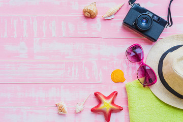 Beach accessories including sunglasses, sunscreen, hat beach, shell, starfish and retro camera on bright pink pastel wooden background for summer holiday and vacation concept.