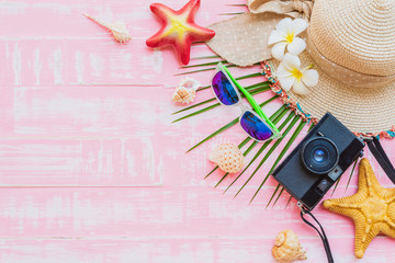 Beach accessories including sunglasses, sunscreen, hat beach, shell, green coconut palm leaves tree and retro camera on bright pink pastel wooden background for summer holiday and vacation concept.