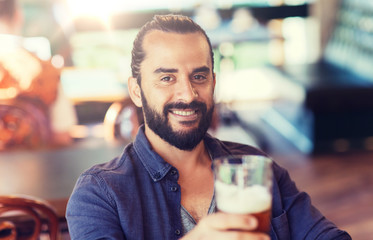 people, drinks, alcohol and leisure concept - happy young man drinking beer at bar or pub