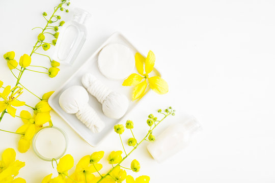 Bright spa background: candles and thai massage herbal bags with bottles and yellow flowers on white. Health, skin treatment concept