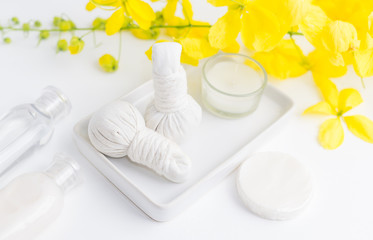 Bright spa background: candles and thai massage herbal bags with bottles and yellow flowers on white. Health, skin treatment concept
