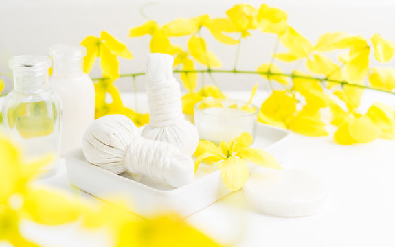 Bright spa background: candles and thai massage herbal bags with bottles and yellow flowers on white. Health, skin treatment concept