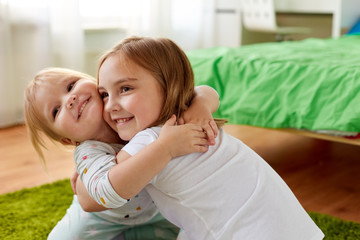 childhood, family, expressions and people concept - happy little girls or sisters hugging at home