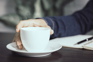 close up hand holding cup of coffee on working table