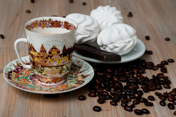 bright cup with coffee beans and sweets on a wooden table