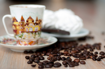 bright cup with coffee beans and sweets on a wooden table