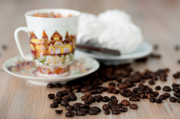 bright cup with coffee beans and sweets on a wooden table