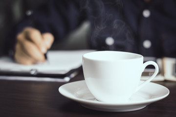 close up hot cup of coffee and businessman working background