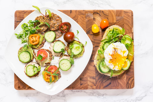 Raw healthy burger with avocado, cucumbers, poached egg and multigrain bread and  veggy crackers with guacamole, hummus, cherry tomatoes, cucumbers and sprouted baby greens. Superfood snack concept