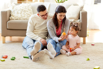 family, holidays and people concept - mother with birthday cupcake, father and happy little daughter at home party