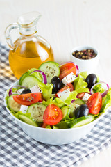Fresh Greek salad made of cherry tomato, ruccola, arugula, feta, olives, cucumbers, onion and spices. Caesar salad in a white bowl on wooden background. Healthy organic diet food concept.
