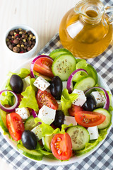 Fresh Greek salad made of cherry tomato, ruccola, arugula, feta, olives, cucumbers, onion and spices. Caesar salad in a white bowl on wooden background. Healthy organic diet food concept.