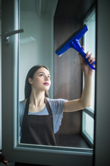 Fototapeta na wymiar Young Happy Woman Wearing Yellow Gloves Cleaning Window With Squeegee And Spray Bottle. Cleaning company