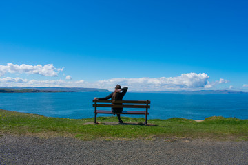 young woman with dark hair sitting on bench opposite ocean and enjoy beautiful view. coast of northern ireland 