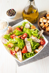 Fresh salad made of tomato, ruccola, chicken breast, eggs, arugula, crackers and spices. Caesar salad in a white, transparent bowl on wooden background