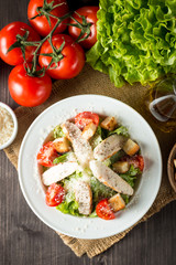 Fresh salad made of tomato, ruccola, chicken breast, eggs, arugula, crackers and spices. Caesar salad in a white, transparent bowl on wooden background