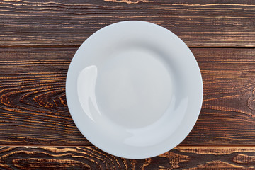 White empty plate, top view. Porcelain plate on brown wooden background.