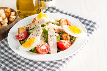 Fresh salad made of tomato, ruccola, chicken breast, eggs, arugula, crackers and spices. Caesar salad in a white, transparent bowl on wooden background