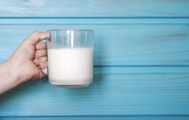 Hand of a child with a glass of fresh milk against a blue wooden wall