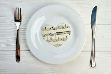 Paper heart with musical notes on white plate. Table setting with plate, fork and knife. Music and love concept.