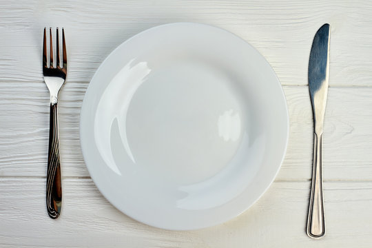 Empty plate, fork and knife. Kitchen utensil on white wooden table, top view. Restaurant table setting.