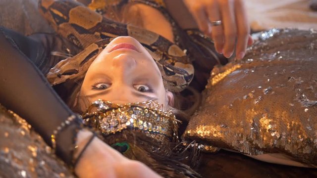 Python crawling on the face of young female dancer in bright costume