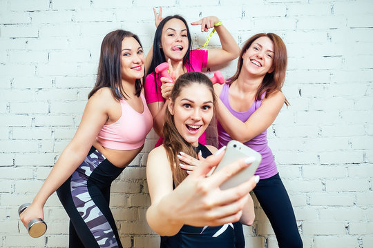 four beautiful and young women taking pictures on the phone in sports clothes in the gym. girlfriends woman do selfie in sportswear