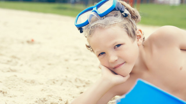 Little boy with snorkeling equipment lying on tropical beach and posing. Kids having fun during summer vacation.