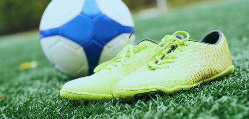 Soccer ball and football boots on green grass