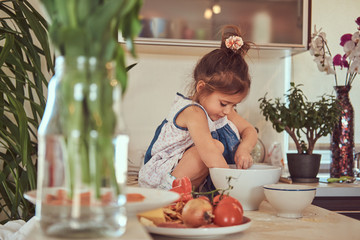 Sweet little cute girl learns to cook a meal in the kitchen.
