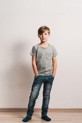 a cute boy stands next to white wall, grey t-shirt, blue jeans, hands in pockets © Kalinova Olena