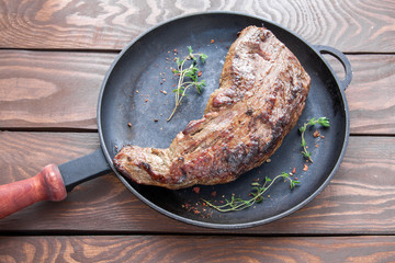 roast beef steak sprinkled with herbs and spices and twigs of thyme on a black iron frying pan on a...
